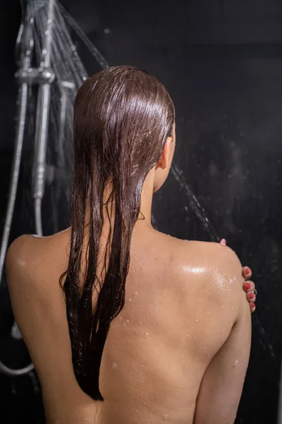 Naken ung kvinna njuter av rinnande vatten ta hand om sin hud. svart bakgrund — Stockfoto