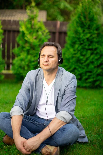 Gestresster Mann mit Kopfhörern, der im Freien chillt und mit geschlossenen Augen Musik hört — Stockfoto