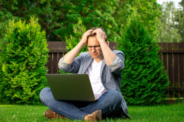 Hombre de negocios desesperado. El hombre molesto se sienta en la hierba con el ordenador portátil agarrando la cabeza — Foto de Stock