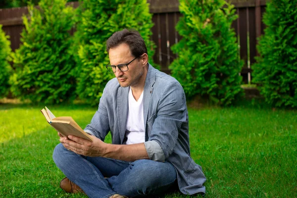 Yetişkin bir adam kitap okuyarak rahatlıyor, iş adamı elinde kitapla parkta oturuyor. — Stok fotoğraf