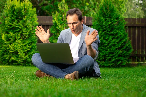 Hombre de negocios alegre se sienta al aire libre, mira con sorpresa en la pantalla del ordenador portátil, ganancias — Foto de Stock