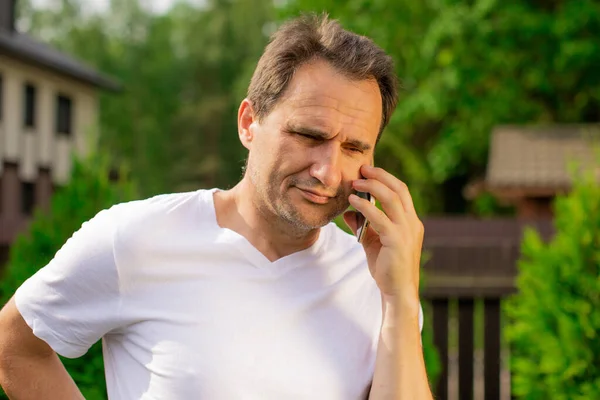 Retrato no emocional del hombre de 40 años sin afeitar en camiseta blanca hablando por teléfono — Foto de Stock
