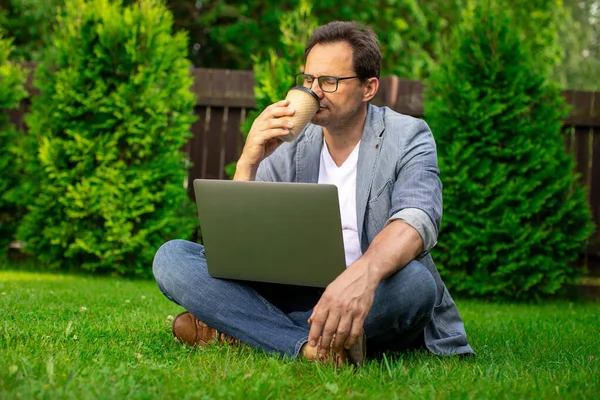 Atractivo hombre de negocios de mediana edad descansando al aire libre con el ordenador portátil bebiendo café — Foto de Stock