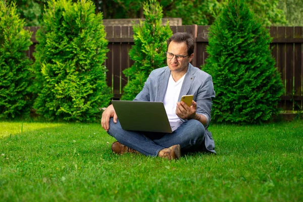 Empresario de mediana edad trastornado se sienta al aire libre con el ordenador portátil y el teléfono móvil — Foto de Stock