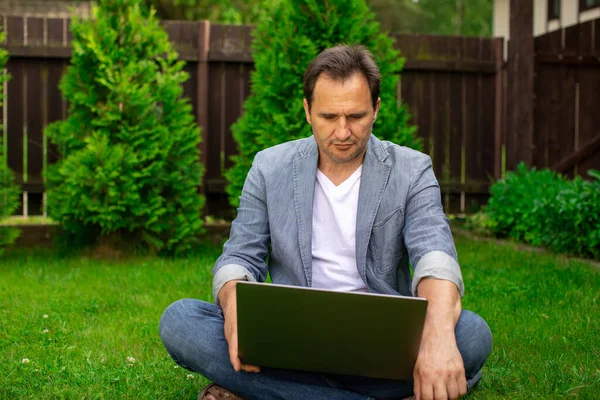 Middle aged man sits outdoors watching video online, business training courses
