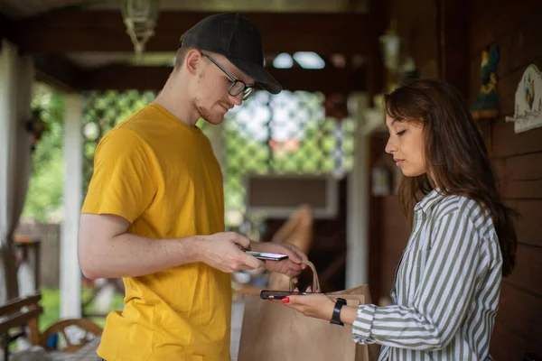 Mujer joven usando teléfono inteligente para pagar su pedido de repartidor hombre — Foto de Stock