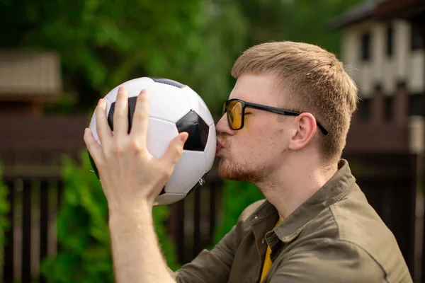 Happy male football fan kisses soccer ball, successful bet on sports, betting