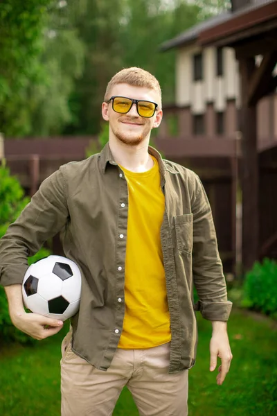 축구 공을 들고 웃으며 카메라를 보고 있는 젊고 잘생긴 남자의 모습 — 스톡 사진