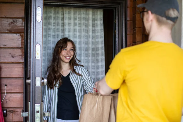 uniformed delivery man handing paper bags of food to Attractive smiling girl