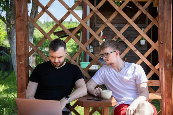 Los hombres jóvenes trabajan remotamente al aire libre en coutryside, dos colegios masculinos usando el ordenador portátil — Foto de Stock