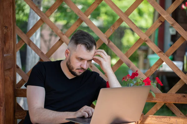 Joven empresario atractivo trabaja remotamente desde casa al aire libre utilizando el ordenador portátil — Foto de Stock