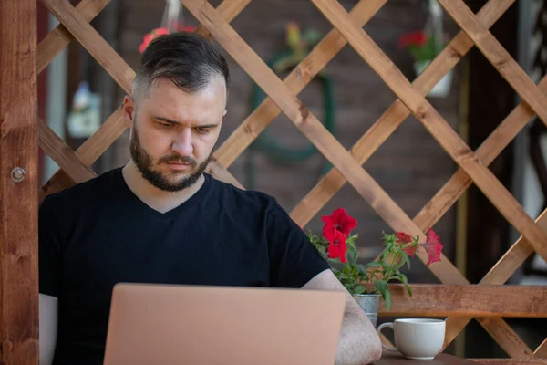 Düşünceli sakallı adam yazın açık havada tahta pergola üzerinde dizüstü bilgisayara bakar. — Stok fotoğraf