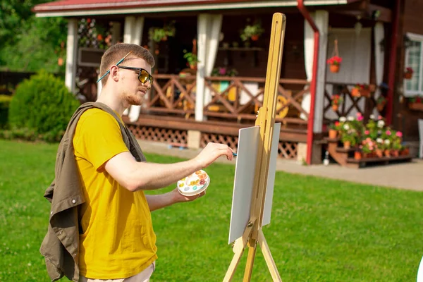 Joven pinta pintura fuera de su casa de campo. Sesión de verano al aire libre — Foto de Stock