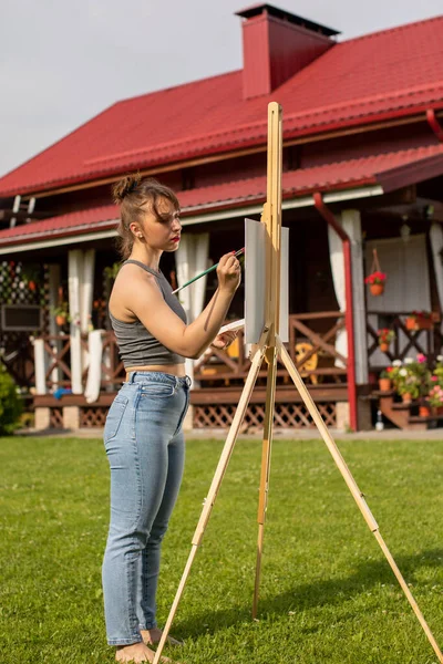 Όμορφη γυναίκα καλλιτέχνης ζωγραφική εικόνα στο καβαλέτο έξω στην πίσω αυλή — Φωτογραφία Αρχείου