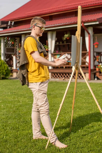 Bonito artista masculino pintura quadro no cavalete fora, inspiração de verão — Fotografia de Stock