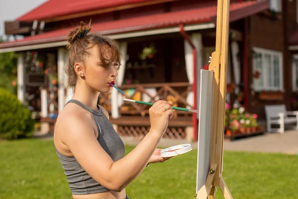 Atractiva chica pintura sosteniendo cepillo en sus dientes y paleta en la mano — Foto de Stock