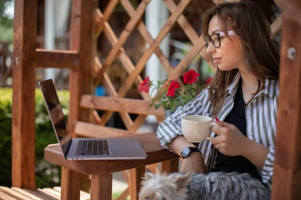 Chica con estilo mira a la computadora portátil que se comunica en la red social en la pérgola de madera — Foto de Stock