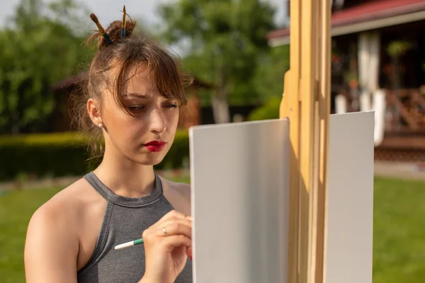 Ελκυστική μελαχρινή κοπέλα ζωγραφίζει easel ζωγραφική έξω από το σπίτι της χώρας — Φωτογραφία Αρχείου