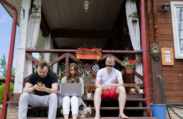 Felices jóvenes amigos se sientan en la terraza de madera con el ordenador portátil, smartphone, reloj inteligente — Foto de Stock