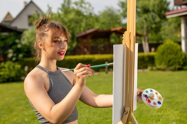 Bastante sonriente artista chica con borlas como horquillas está pintando al aire libre — Foto de Stock