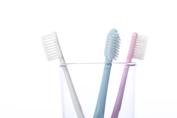 Close up three toothbrushes in transparent glass isolated on white background — Stock Photo, Image