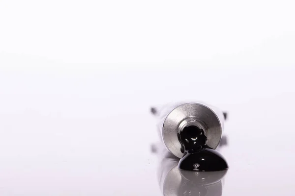 Ściśnięta rurka z farbą akrylową, kolor czarny, odbity w powierzchni stołu — Zdjęcie stockowe