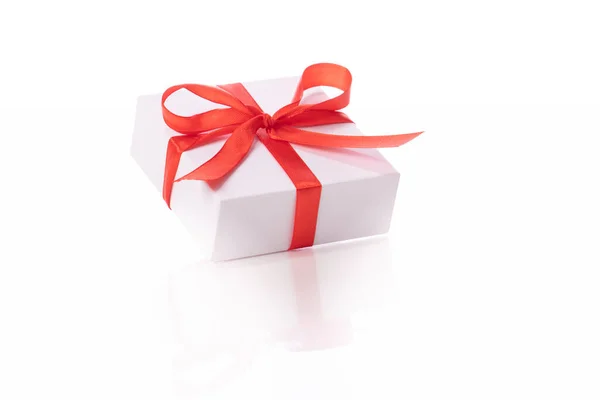 Gift box tied with red satin ribbon and bow reflected in glass table surface Stock Picture