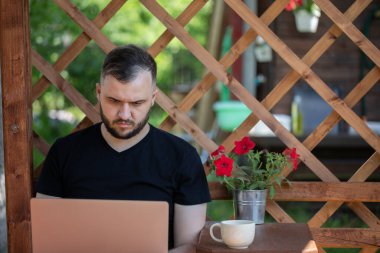 Uzak mesafe çalışma konsepti. Genç adam dizüstü bilgisayarla ahşap pergola üzerinde çalışıyor.