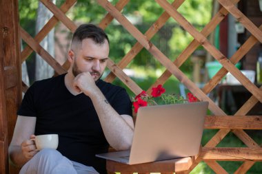 Mesafe çalışma kavramı. Düşünceli genç adam Pergola 'da dizüstü bilgisayarla çalışıyor.