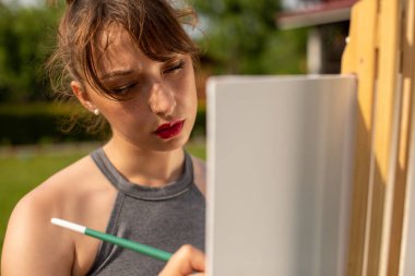 Parkta tuvale resim yapan güzel kadın ressamın yakın portresi.