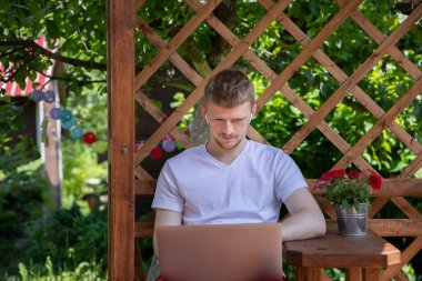Erkek öğrenci terasta oturur. Webinar 'ı izler. Serbest çalışır.