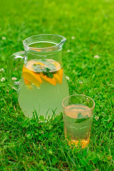 Frische Sommer-Limonade im Glas mit Orangen und Minze auf der grünen Wiese im Freien — Stockfoto