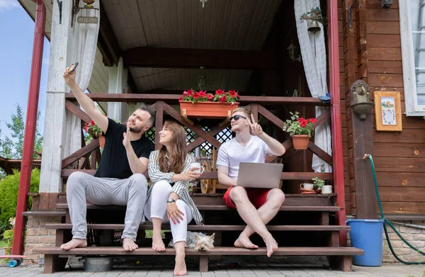 İki adam ve kadın terasta oturmuş selfie çekiyorlar. Dijital, aygıtlar