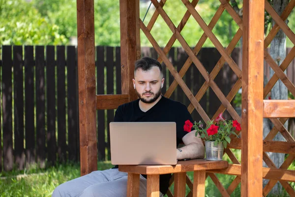 Snygg ung man avstånd arbetar med bärbar dator utomhus på trä pergola — Stockfoto