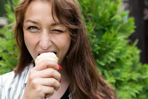 Outdoor close up portrait of playful beautiful woman eating ice cream and winks
