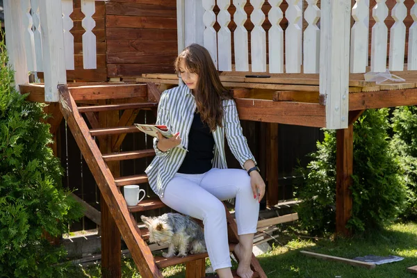 Atractiva mujer con york perro lectura revista en escaleras de madera — Foto de Stock