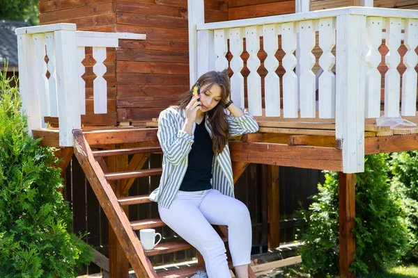 Mujer joven descansando al aire libre en el porche de la casa de campo, hablando por teléfono móvil — Foto de Stock