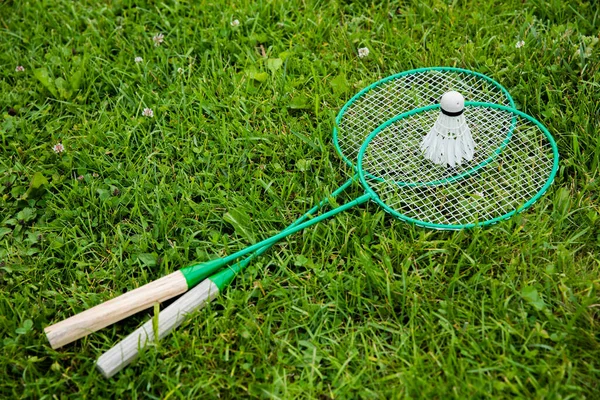 Badminton rackets and shuttlecock on green grass, outdoors summer hobby