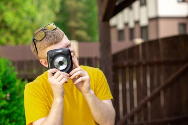 Genç yaratıcı yakışıklı adam dışarıda eğleniyor, kamerayla fotoğraf çekiyor.
