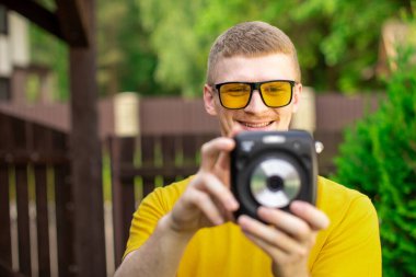 Sarı tişörtlü, genç, mutlu hippi adam kamerayla fotoğraf çekiyor.
