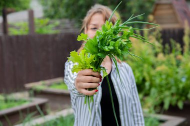 Genç kadın elinde yeşil soğan, maydanoz ve salata yapraklarından oluşan bir buket tutuyor.