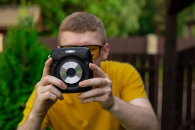 Sarı giysili genç yaratıcı adam fotoğraf makinesiyle fotoğraf çekiyor.