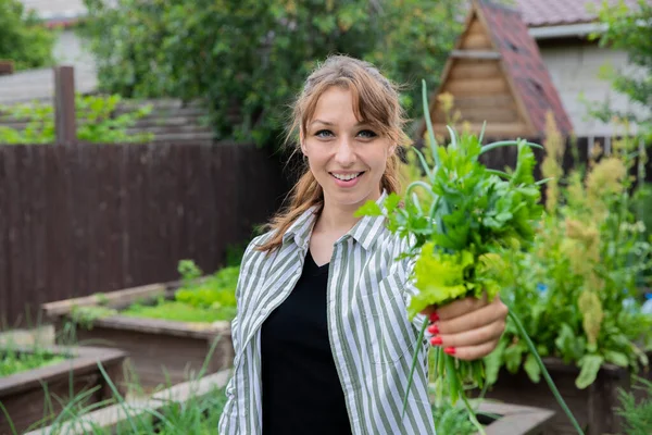 Sonriente mujer sostiene ramo de cebollas verdes, perejil y ensaladas en el jardín — Foto de Stock