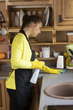 Genç kadınlar mutfak atölyelerini sprey kullanarak temizler, masayı süngerle yıkarlar.