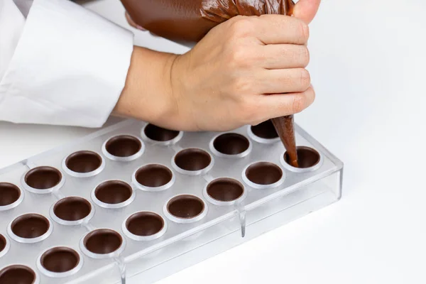 Chocolatier gießt Pralinenfüllung in Schokoladenform und bereitet belgische Bonbons vor — Stockfoto