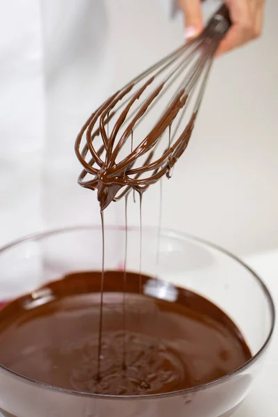 Nahaufnahme rührt milchgeschmolzene Schokolade in Glasschüssel mit Schneebesen, weißer Hintergrund — Stockfoto