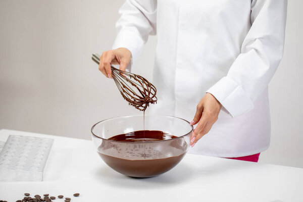 Closeup chocolatier pouring dark melted chocolate with whisk on white background