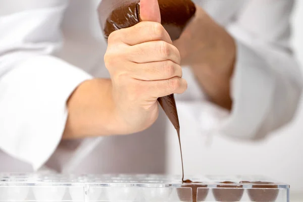 Nahaufnahme Chocolatier gießt dunkle Schokolade in Form von Süßigkeiten mit Teigtasche — Stockfoto