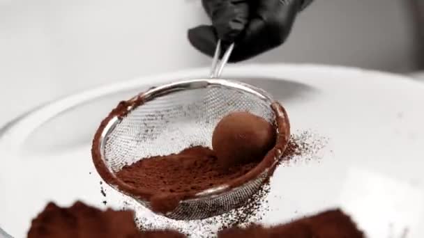 Pastelero vierte caramelos de trufa en polvo de cacao utilizando colador lento mo primer plano — Vídeos de Stock