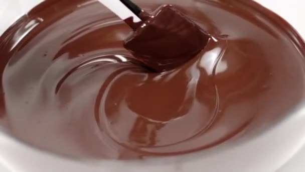 Closeup mexendo misturando leite derretido chocolate em tigela de vidro no fundo branco — Vídeo de Stock